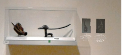 Two statues in a glass case against a wall. On the right,
                  there are two hologram images of related art pieces.