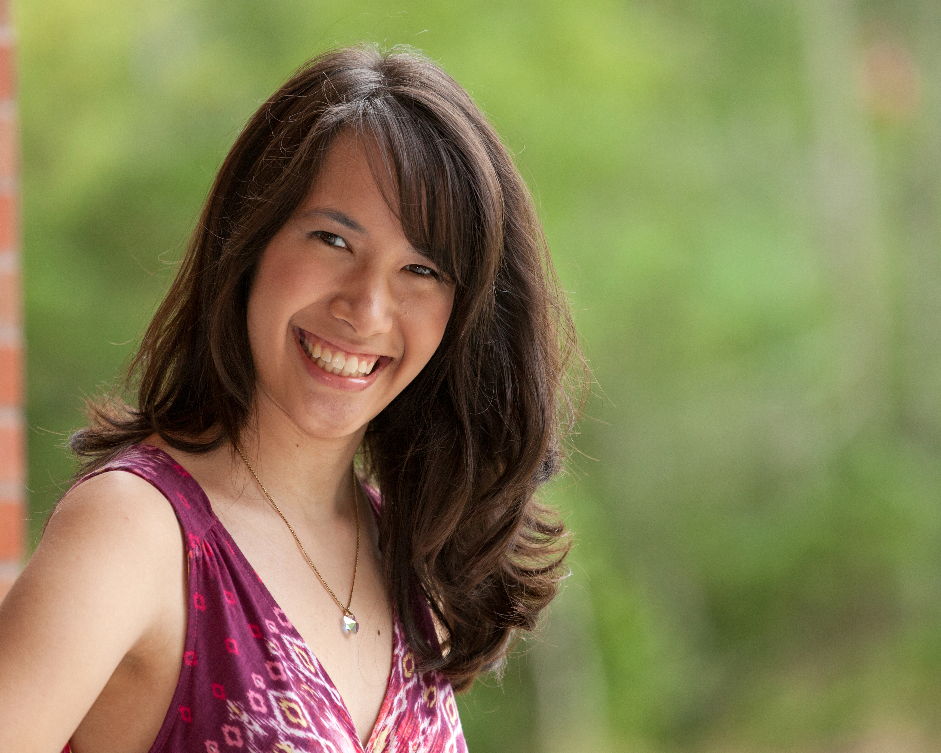 Dana Hsiao smiles infront of
            a brick column and a green background.