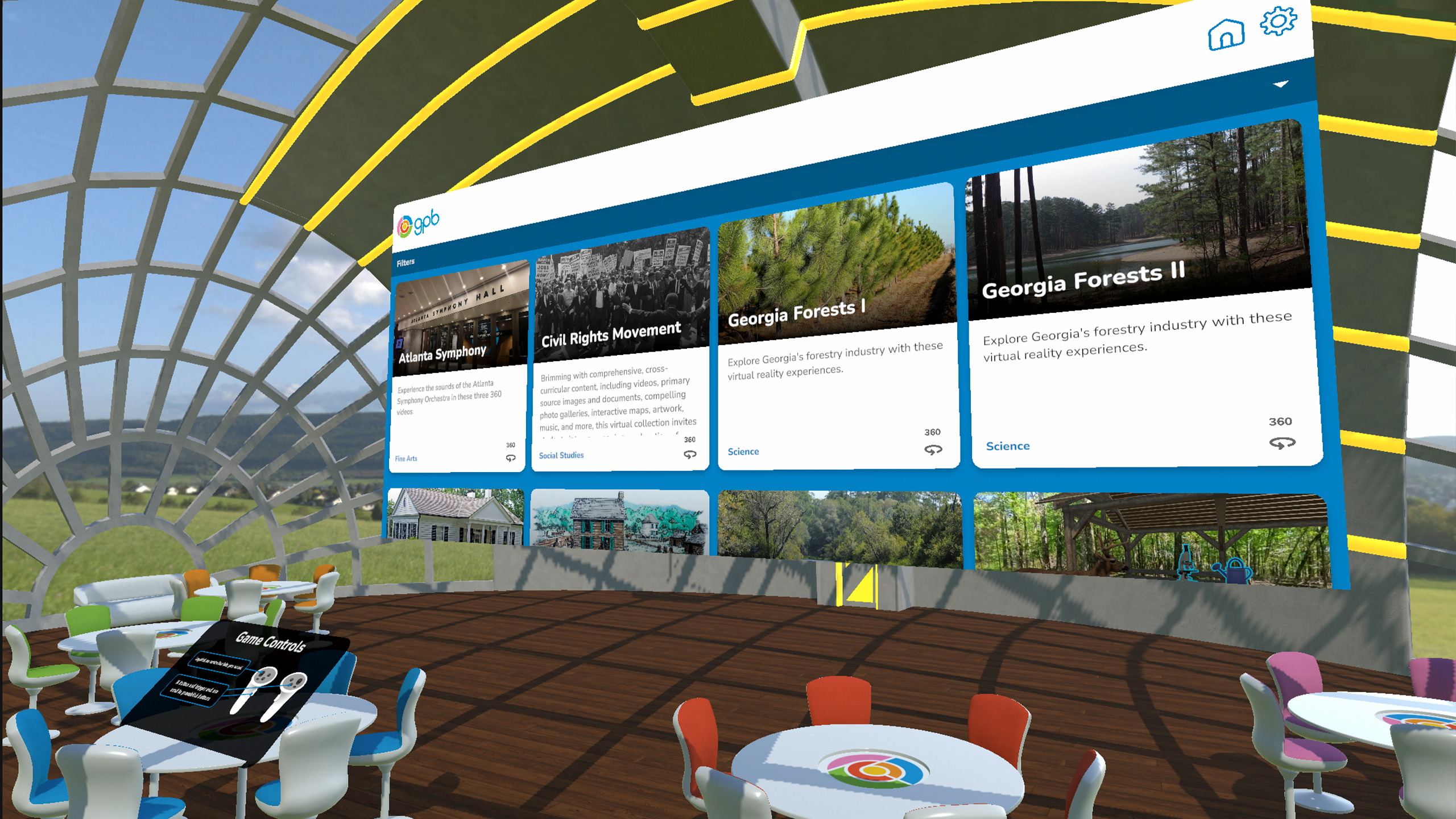 Virtual reality hub menu: A large domed room with the roof and walls made of glass sitting in a field.
                    There are several round tables surrounded by chairs. One table has a black panel showing the game controls
                    for virtual reality. On the far side of the room is a large screen with the menu showing the first four modules: 
                    Atlanta Symphony, Civil Rights Movement, Georgia Forests 1, and Georgia Forests 2.